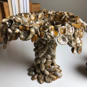 May include: A ceramic vase shaped like a mushroom, made from small, irregular pieces of ceramic in shades of brown, beige, and white.