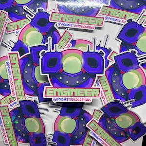 May include: A collection of die-cut stickers featuring a purple and green robot character with antennas. The design includes the text ENGINEER and @PRISMSTUDIODESIGNS in a light green font. The stickers have a glossy finish with a holographic effect.