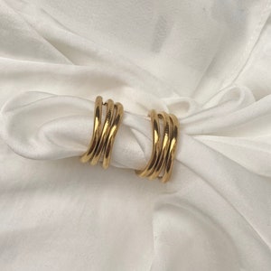 May include: A pair of gold hoop earrings with a multi-layered design. The earrings are made of a smooth, shiny metal and have a simple, elegant style.