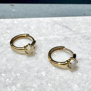 May include: A pair of gold hoop earrings with a white opal gemstone on each hoop.
