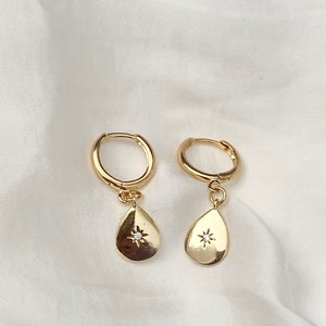 May include: A pair of gold hoop earrings with a small teardrop pendant featuring a star with a clear stone in the center.
