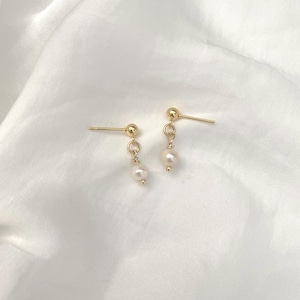 May include: A pair of gold stud earrings with small white pearl drops.