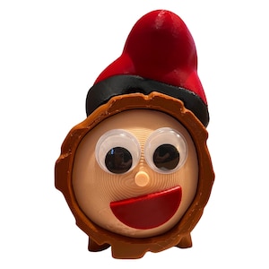 Könnte beinhalten: Ein brauner Holzscheit mit einem roten und schwarzen Hut, Kulleraugen und einem roten Mund. Der Scheit ist eine Weihnachtsdekoration.