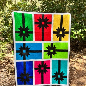 May include: A colorful quilt with a geometric pattern of presents. The quilt is made of green, red, yellow, blue, and pink fabric with black accents.