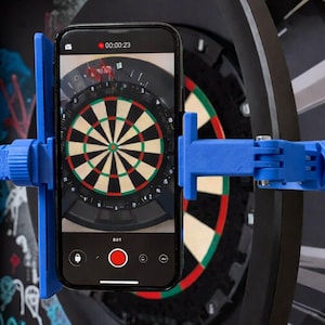 Może przedstawiać: Smartfon nagrywa tarczę do darta, trzymaną na miejscu przez niebieski wspornik montażowy. Tarcza do darta jest czarna z czerwonymi, zielonymi i białymi sekcjami. Ekran telefonu wyświetla tarczę i timer. Wspornik jest przymocowany do tarczy.