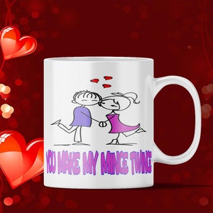 May include: White ceramic coffee mug with a black and purple illustration of a couple holding hands. The text "You make my mince thing" is printed in purple on the mug.