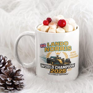 Op de afbeelding: Witte keramische mok gevuld met marshmallows en rode bessen. De mok heeft een ontwerp met de tekst "LANDO NORRIS WORLD CHAMPION 2025" en een Formule 1 raceauto-afbeelding. De mok heeft een handvat.