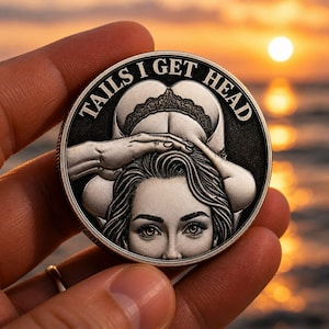 Può includere: Una moneta d'argento con la scritta "TAILS I GET HEAD" sul bordo. La moneta presenta il volto di una donna e la raffigurazione di una persona che si china. La moneta è tenuta in mano su uno sfondo di tramonto.