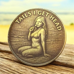 May include: A round, bronze-colored coin with the text "TAILS I GET HEAD" around the edge. The coin features an engraved image of a woman in a bikini holding a lollipop. The background shows a beach scene.