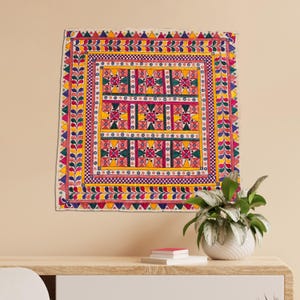 May include: A colorful embroidered wall hanging with a geometric pattern in shades of red, yellow, green, blue, and pink. The design features a repeating motif of stars and squares.