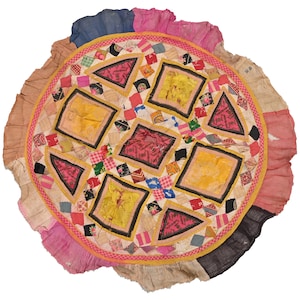 Peut inclure: Une courtepointe ronde en patchwork avec un motif central de carrés et de triangles dans des tons de rose, jaune et bleu. La courtepointe est entourée d'une bordure à volants rose et beige.