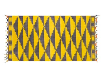 May include: A yellow and dark blue woven rug with a geometric diamond pattern. The rug has fringe on the ends.