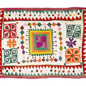 Pode incluir: Um tecido de algodão branco com um padrão geométrico colorido. O padrão apresenta quadrados, diamantes e círculos em tons de vermelho, verde, laranja, rosa e roxo. O tecido é decorado com flores bordadas.