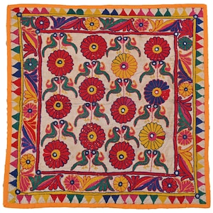 Peut inclure: Textile carré avec un fond crème, présentant un motif répété de fleurs rouges, jaunes et bleues, et d'oiseaux verts. La bordure est orange avec des motifs géométriques et floraux colorés. Le textile est probablement fait à la main.