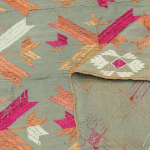 Puede incluir: Primer plano de una tela gris con diseños bordados en rosa, naranja y blanco. La tela tiene una textura tejida y un brillo sutil.