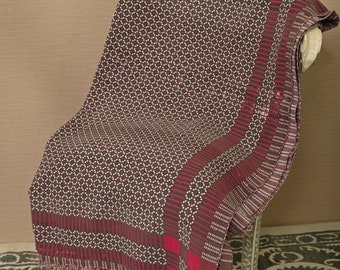 May include: A red and black patterned throw blanket with white accents. The blanket is folded and draped over a chair.