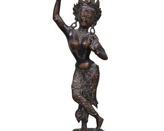 Op de afbeelding: Een bronzen beeld van een dansende vrouw met ingewikkelde details en een kroon. Het beeld staat op een ronde basis met decoratieve accenten.