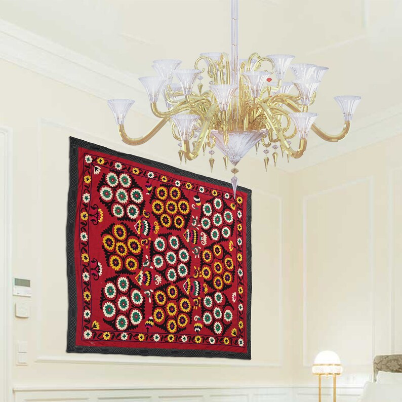 K&ouml;nnte beinhalten: Eine rote, schwarze und wei&szlig;e bestickte Wandteppich mit einem floralen Muster h&auml;ngt an einer wei&szlig;en Wand. Der Wandteppich zeigt ein sich wiederholendes Muster aus stilisierten Blumen und Kreisen.