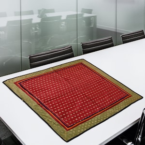 Puede incluir: Un camino de mesa rojo con un borde estampado en dorado y negro. El camino de mesa está sobre una mesa blanca en una sala de conferencias.