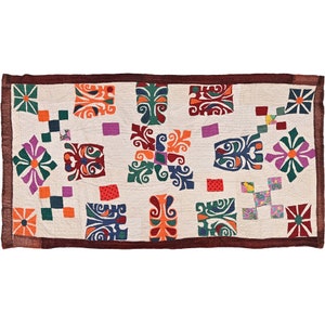 Könnte beinhalten: Eine weiße Baumwolldecke mit braunem Rand. Die Decke ist mit einem Patchwork-Muster aus bunten Quadraten und geometrischen Mustern verziert. Die Muster sind in Rot-, Orange-, Gelb-, Grün-, Blau-, Lila- und Brauntönen gehalten.