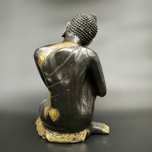 May include: Black and gold Buddha statue sitting in a meditative pose. The statue has intricate details and a serene expression.