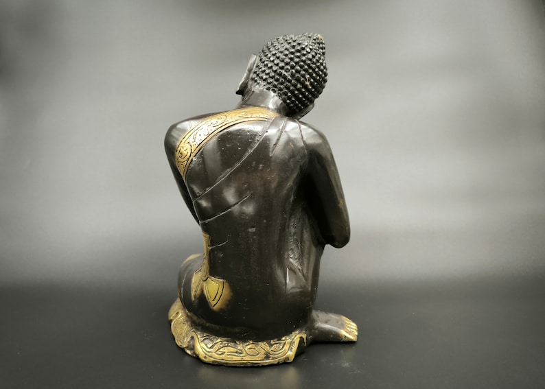 May include: Black and gold Buddha statue sitting in a meditative pose. The statue has intricate details and a serene expression.
