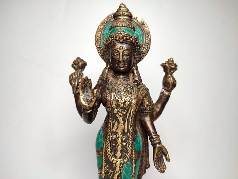 May include: A four-armed bronze statue of a Hindu goddess with a green and gold headdress and intricate details. The statue is standing on a white background.