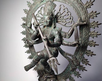 May include: A green bronze statue of a Hindu deity, Shiva, in the Nataraja pose, dancing on a demon. The statue is surrounded by a circular halo with intricate carvings.