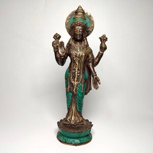 May include: A gold and green metal statue of a Hindu goddess with four arms holding lotus flowers. The statue is standing on a lotus base.