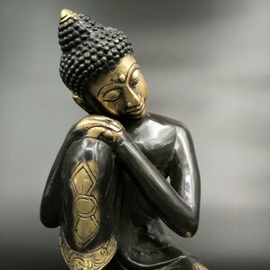 May include: A black and gold statue of a meditating Buddha with his head resting on his hand.