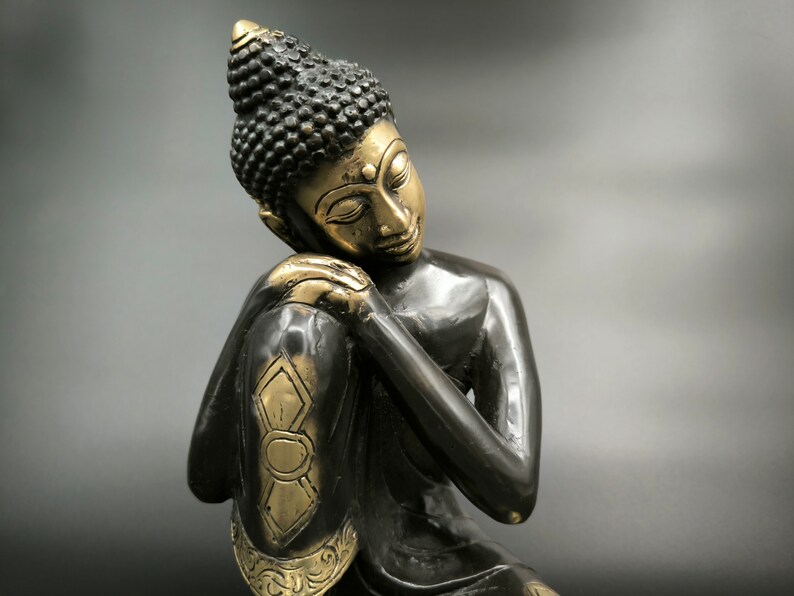 May include: A black and gold statue of a meditating Buddha with his head resting on his hand.