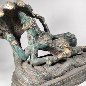 May include: A green bronze statue of the Hindu god Vishnu reclining on a serpent, with a golden crown and a golden serpent hood.