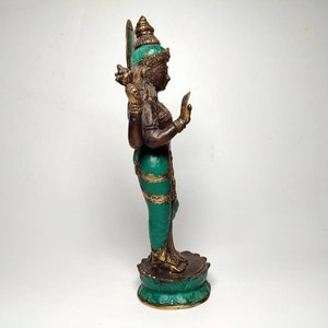 May include: A green and gold colored statue of a Hindu deity with four arms. The statue is standing on a lotus base.