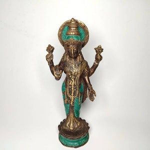 May include: A gold-colored statue of a Hindu deity with four arms, wearing a green and gold headdress and a green and gold robe. The statue is standing on a green and gold base.