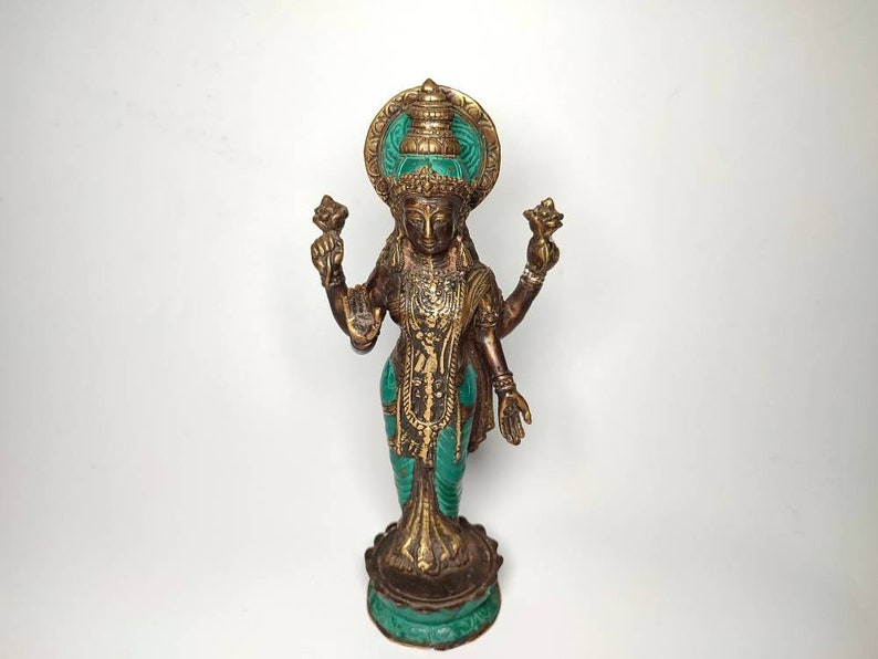 May include: A gold-colored statue of a Hindu deity with four arms, wearing a green and gold headdress and a green and gold robe. The statue is standing on a green and gold base.