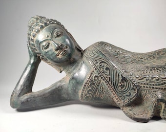 May include: A green bronze sculpture of a reclining Buddha. The Buddha is lying on its side with its head resting on its hand. The sculpture is intricately detailed with a patterned robe.