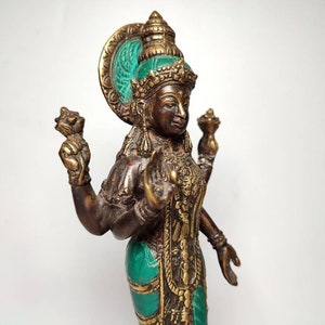 May include: A bronze statue of a Hindu goddess with four arms, wearing a green and gold headdress and a green and gold robe. The statue is holding a lotus flower in one hand and a conch shell in another.