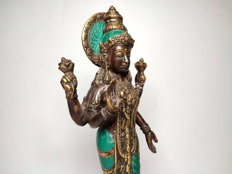 May include: A bronze statue of a Hindu goddess with four arms, wearing a green and gold headdress and a green and gold robe. The statue is holding a lotus flower in one hand and a conch shell in another.