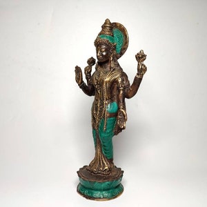 May include: A gold and green metal statue of a Hindu goddess standing on a lotus base. The goddess has four arms and is wearing a green and gold sari.