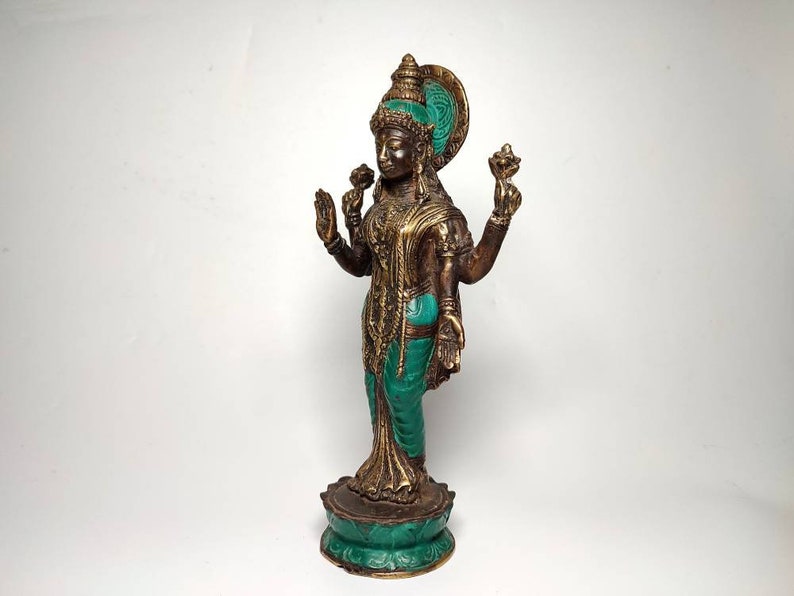 May include: A gold and green metal statue of a Hindu goddess standing on a lotus base. The goddess has four arms and is wearing a green and gold sari.