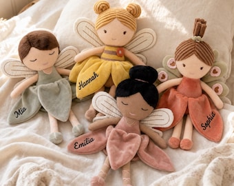 May include: Four plush fairy dolls with embroidered facial features and wings. The dolls are dressed in soft fabric outfits in sage green, yellow, black, and dusty rose, with the names Mia, Hannah, Emilia, and Sophia embroidered on their skirts.