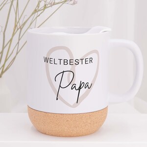 Könnte beinhalten: Weißer Keramikbecher mit Korkboden. Der Becher trägt den Text "WELTBESTER Papa" in Schwarz und ein Herzdesign. Der Becher hat einen weißen Griff und einen weißen Deckel. Der Becher steht auf einer weißen Oberfläche.