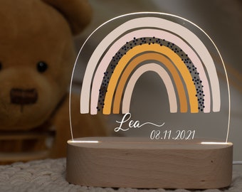 May include: A wooden night light with a clear acrylic rainbow design. The rainbow has a pink, orange, and yellow color scheme with black dots. The night light is personalized with the name "Lea" and the date "08.11.2021".