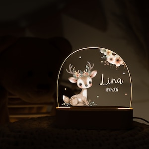 Op de afbeelding: Een houten nachtlampje met een transparante acrylkoepel met een aquarelillustratie van een fawn met een bloemenkrans. De koepel bevat ook de naam "Lina" en de datum "18.04.2018".