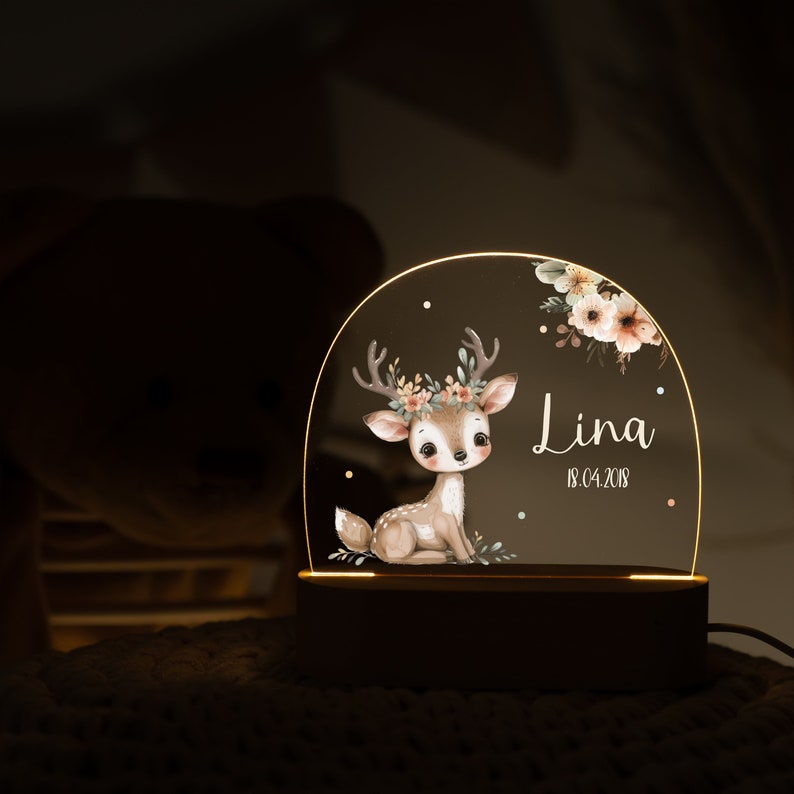 Op de afbeelding: Een houten nachtlampje met een transparante acrylkoepel met een aquarelillustratie van een fawn met een bloemenkrans. De koepel bevat ook de naam "Lina" en de datum "18.04.2018".