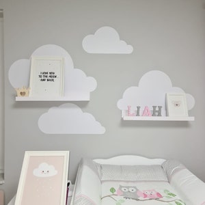 Peut inclure: Une chambre de bébé avec une table à langer blanche et un matelas à langer gris et blanc avec un motif de hibou rose. Le mur est peint en gris et comporte des découpes de nuages blancs et une étagère avec un imprimé encadré qui dit "Je t'aime jusqu'à la lune et retour".