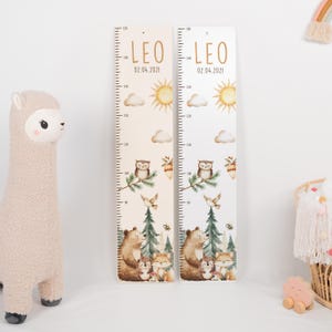 May include: Two vertical wooden growth charts featuring the name LEO and the date 02.04.2021. The charts display a printed forest scene with a bear, fox, owl, sun, clouds, and pine trees, with measurement markings from 80 to 150 cm.