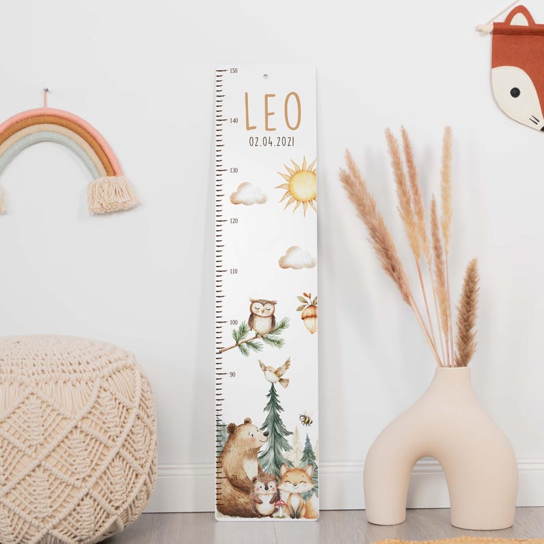 May include: A vertical wooden growth chart featuring the name LEO and the date 02.04.2021. The ruler displays measurements from 90 to 150 cm, decorated with illustrations of a sun, clouds, an owl, a bear, a hedgehog, a fox, and pine trees.