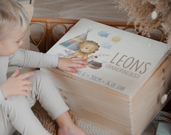 May include: A light-colored wooden keepsake box featuring a printed illustration of a lion, a teepee, clouds, and the sun. The text reads LEONS ERINNERUNGSKISTE, 3500 G, 50 CM, and 14:01 UHR. The box has a smooth, natural wood grain finish.