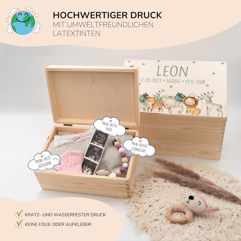 May include: A wooden keepsake box with a light wood finish. The lid is decorated with a colorful illustration of animals and the text "LEON 12.03.2023 - 3600g - 19:11 UHR". The box is open and contains a pink baby sock, a white onesie, a baby rattle, and a sonogram photo. The box is labeled with the text "HOCHWERTIGER DRUCK MIT UMWELTFREUNDLICHEN LATEXTINTEN" and "KRATZ- UND WASSERFESTER DRUCK KEINE FOLIE ODER AUFKLEBER".